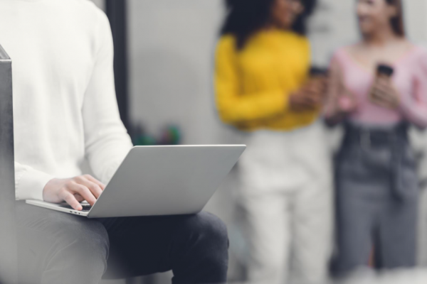 holding a laptop, two women in the background with cell phones